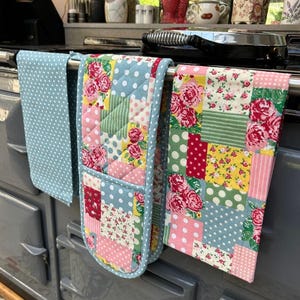 May include: Kitchen textiles including a light blue polka dot tea towel, a patchwork oven glove, and a floral patterned tea towel. The oven glove and tea towel feature floral and polka dot patterns in pink, red, yellow, and green.