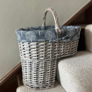 May include: A grey wicker basket with a handle, lined with a grey fabric featuring a white tree pattern. The basket is placed on a staircase with a neutral-toned carpet.