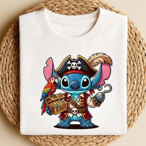 K&ouml;nnte beinhalten: Wei&szlig;es T-Shirt mit einer Cartoon-Figur als Pirat. Die blaue Figur hat gro&szlig;e Ohren, einen Piratenhut mit Totenkopf, eine rote Weste und einen Haken sowie eine Schatzkiste. Ein bunter Papagei sitzt auf der Schulter der Figur.
