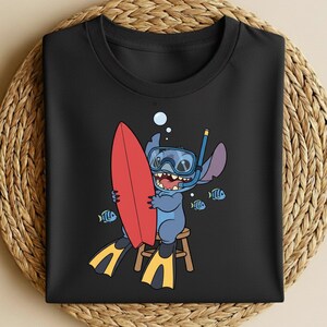 May include: Black t-shirt featuring a cartoon character wearing a snorkel and holding a red surfboard. The character is blue with large ears and is sitting on a small wooden stool. Yellow and black flippers are visible, along with small blue fish.