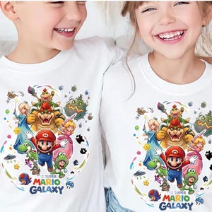 May include: Two white t-shirts with a vibrant graphic of Mario, Bowser, Princess Peach, and other characters from the Super Mario Galaxy game. The text "THE SUPER MARIO GALAXY" is printed at the bottom of the design.
