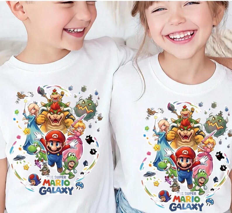 May include: Two white t-shirts with a vibrant graphic of Mario, Bowser, Princess Peach, and other characters from the Super Mario Galaxy game. The text "THE SUPER MARIO GALAXY" is printed at the bottom of the design.