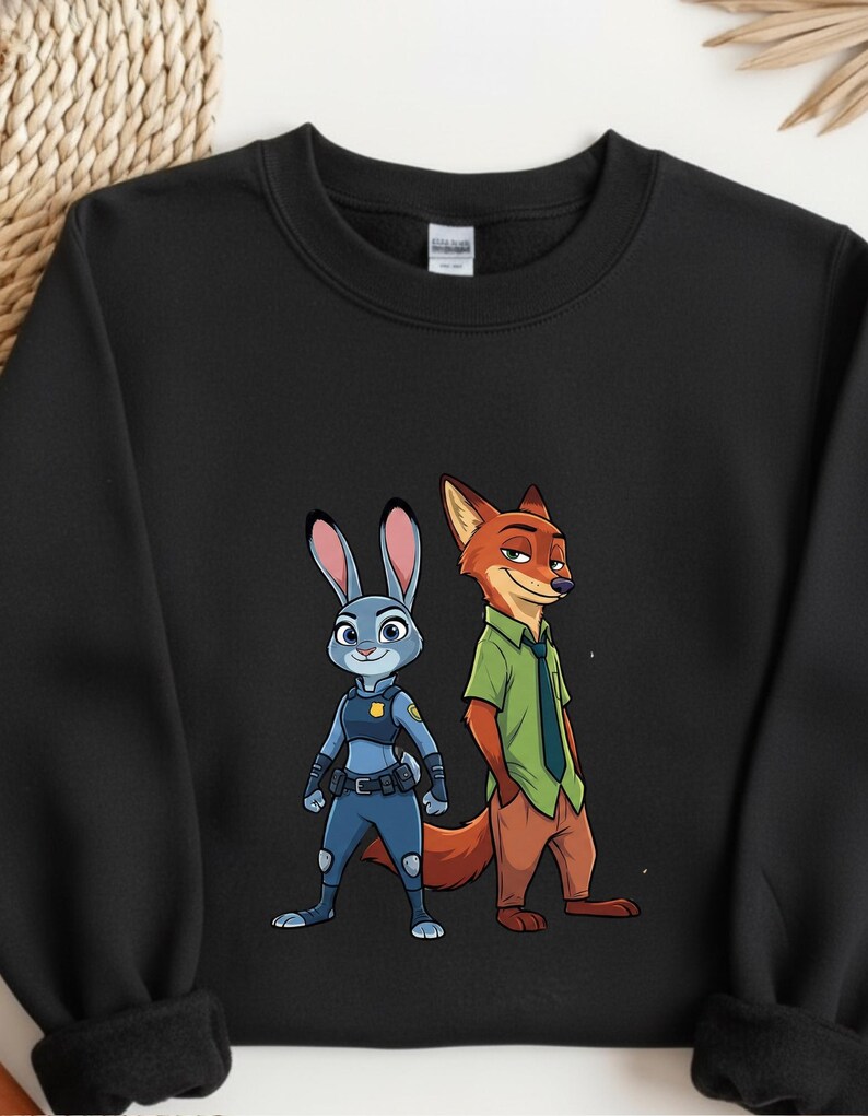 以下が含まれることがあります： 黒いクルーネックのスウェットシャツ。青いウサギのジュディ・ホップスと赤いキツネのニック・ワイルドの漫画イラストが描かれています。ジュディは警察の制服を着ており、ニックは緑のシャツとネクタイを着ています。スウェットシャツは柔らかい素材で作られています。
