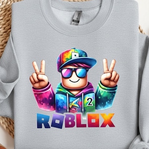 Puede incluir: Sudadera gris claro con un personaje de dibujos animados colorido con gafas de sol y un signo de la paz. El personaje lleva un gorro y una sudadera con capucha de arco&iacute;ris. La palabra "ROBLOX" est&aacute; impresa en la parte inferior.