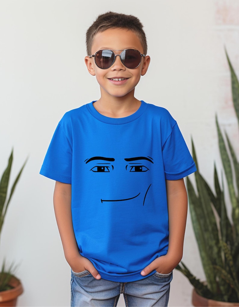 May include: A blue t-shirt featuring a smiling face graphic. The graphic is a simple black outline of eyes and a mouth. The shirt is worn by a person wearing sunglasses and blue jeans.