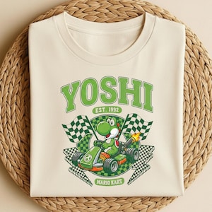 May include: Cream-colored t-shirt featuring a green Yoshi character in a green go-kart, with checkered flags and the text "YOSHI EST. 1992 MARIO KART". The design is centered on the shirt.