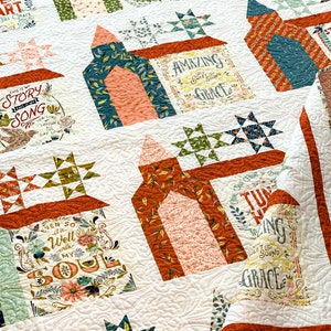 May include: A white quilt with a patchwork design featuring various colorful fabrics with floral patterns and text. The text includes phrases like "This is my story song", "Amazing Grace", "Even so it is well with my soul", and "Turning the sound of Grace".