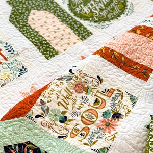 May include: A white quilt with a variety of colorful fabric squares. The squares feature floral patterns, geometric designs, and text. The text includes the phrases "All to the Blessed Savior" and "Even so it is Well with my Soul".
