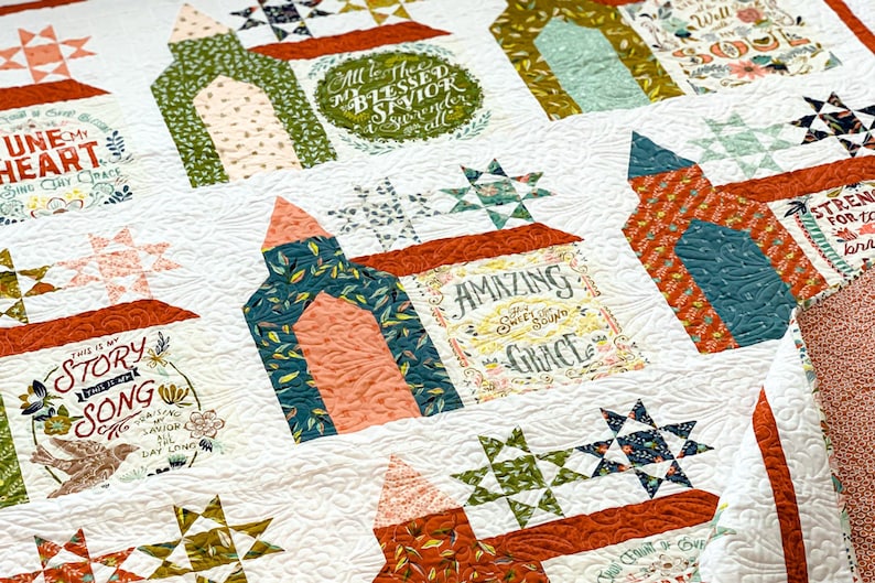 May include: A white quilt with a patchwork design featuring various colors and patterns. The quilt includes several blocks with text, including "This is my Story Song", "Amazing Grace", "Tune My Heart", and "All to Thee My Blessed Savior".