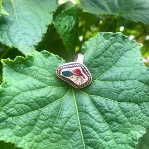 Può includere: Un anello d'argento con una pietra verde, rossa e bianca incastonata in una montatura d'argento. La pietra ha una forma irregolare e un aspetto naturale e organico.