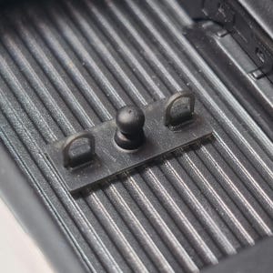 May include: A black metal hitch ball with two D-rings attached to a rectangular plate. The hitch ball is mounted on a black, textured surface, likely a truck bed.