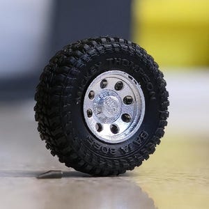 Może przedstawiać: Czarna opona terenowa ze srebrną felgą. Opona ma wytłoczone napisy "MICKEY THOMPSON" i "BAJA BOSS" na boku. Felga ma wiele okrągłych otworów.