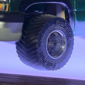 May include: Close-up of a green truck's front wheel. The black tire has a deep tread pattern and the words "ProPuller" and "Full Pull" are visible on the sidewall. The wheel is set against a blue background.