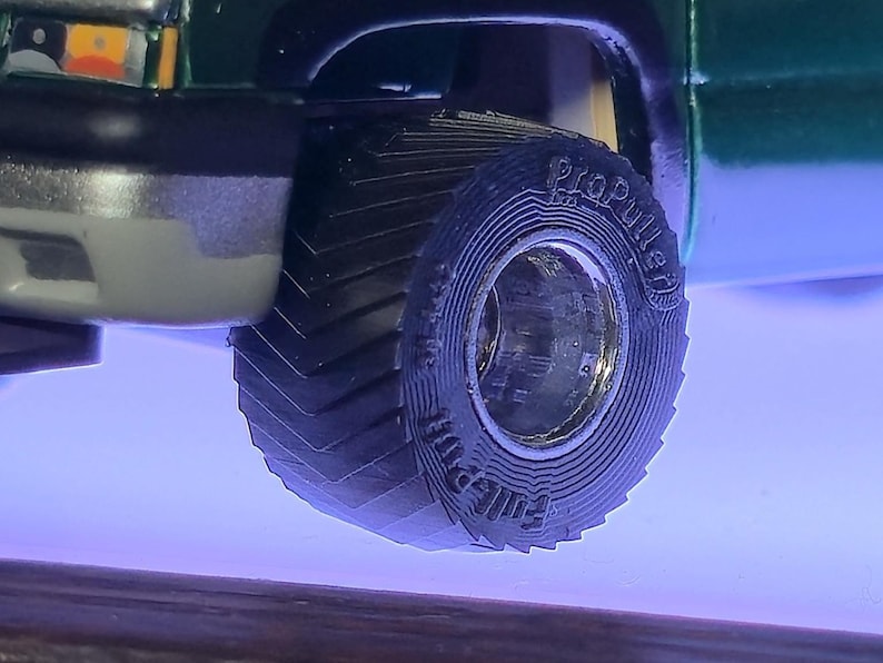 May include: Close-up of a green truck's front wheel. The black tire has a deep tread pattern and the words "ProPuller" and "Full Pull" are visible on the sidewall. The wheel is set against a blue background.