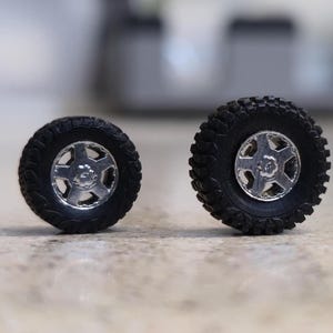 Pode incluir: S&atilde;o apresentados dois pneus pretos para ve&iacute;culos off-road com jantes prateadas. Os pneus t&ecirc;m um padr&atilde;o de piso robusto e as jantes apresentam um design de cinco raios. Os pneus s&atilde;o provavelmente para um carro ou cami&atilde;o modelo.