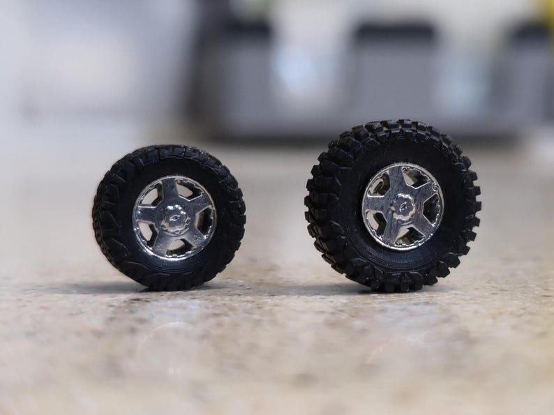 Pode incluir: S&atilde;o apresentados dois pneus pretos para ve&iacute;culos off-road com jantes prateadas. Os pneus t&ecirc;m um padr&atilde;o de piso robusto e as jantes apresentam um design de cinco raios. Os pneus s&atilde;o provavelmente para um carro ou cami&atilde;o modelo.