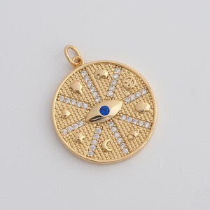 May include: Gold-colored pendant with an eye design, featuring a blue center and surrounding embellishments. The round pendant includes small star, moon, and cloud shapes, and is adorned with small, clear stones. A small loop is at the top for a chain.