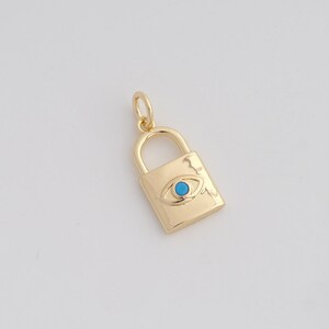 May include: Gold-colored padlock charm with a turquoise eye design. The charm has a rectangular body with a curved top and a small loop for attaching to a chain or bracelet. The eye is centered on the padlock.