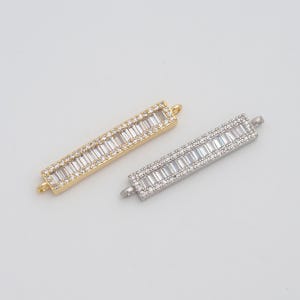 May include: Two rectangular jewelry connectors. One is gold-toned with clear rectangular stones and the other is silver-toned with similar stones. Each has small loops on either end for attachment.