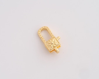May include: A gold-colored rectangular clasp with a floral design on the front. The clasp has a rectangular loop and a small lever to open and close it. The clasp is likely used for jewelry making or as a decorative element.