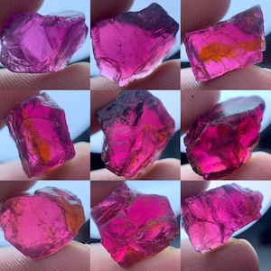 May include: Nine rough-cut, vibrant pink gemstones with varying shapes and sizes. The stones display a range of hues, from deep magenta to lighter shades, with some showing internal orange and brown inclusions. The raw, natural appearance of the stones is emphasized.