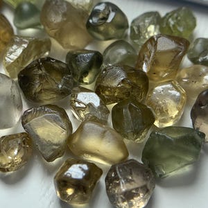 Puede incluir: Una colección de piedras preciosas verdes y marrones, talladas a facetas, sueltas. Las piedras son de varios tamaños y formas, algunas tienen una forma más redondeada y otras una forma más angular.