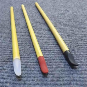 May include: Three long, slender tools with light yellow handles. Each tool features a distinct tip: one is translucent white, one is solid red, and one is solid black. The tips are curved and shaped for precision work, attached to the yellow shafts.