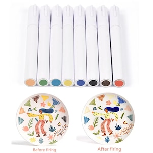 May include: Set of eight ceramic paint markers with white barrels and colored tips. The colors are orange, green, blue, yellow, dark blue, black, brown, and red. The markers are shown next to two ceramic plates, one with a design before firing and one with the same design after firing.