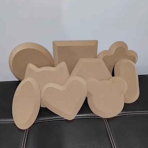 Może przedstawiać: Kolekcja różnych jasnobrązowych drewnianych kształtów, w tym koło, kwadrat, sześciokąt, chmura, owal, kot, serce i niedźwiedź. Kształty są ułożone na czarnej powierzchni.