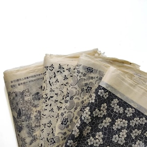May include: Several sheets of patterned paper with a vintage appearance. The designs feature floral, paisley, and text-based patterns in black and white. The paper has a slightly aged, off-white colour.