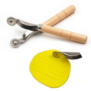 Puede incluir: Dos crimpadoras de pastelería de acero inoxidable y madera con mangos de madera. Las crimpadoras tienen una rueda con borde dentado. Se muestra un círculo amarillo de masa con marcas de crimpado de la herramienta.