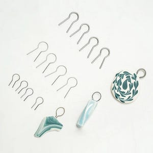 Pode incluir: Um conjunto de argolas de salto prateadas, perfeitas para fazer joias. A imagem também mostra três pingentes de argila polimérica diferentes, um com um padrão de espiral, outro com um design de folha e outro com um padrão geométrico.