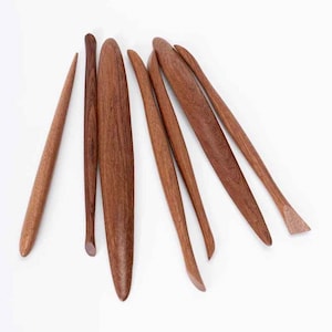 Puede incluir: Colección de siete herramientas de cerámica de madera de varias formas y tamaños. Las herramientas son de un rico color marrón y parecen estar hechas de madera dura. Están dispuestas sobre una superficie blanca, mostrando sus diferentes formas.