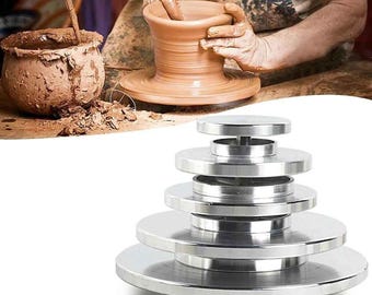 May include: A potter works on a clay pot, with a stack of silver metal pottery wheel bats in the foreground. The clay pot is light brown, and the wheel bats are various sizes.