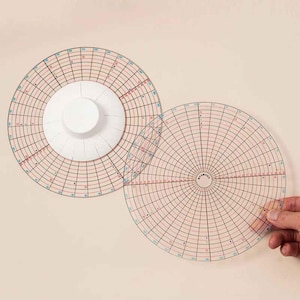 May include: Two circular, transparent plastic quilting templates featuring black grid lines, red and blue numerical markings, and radial degree measurements. One template includes a white, circular center knob for handling.