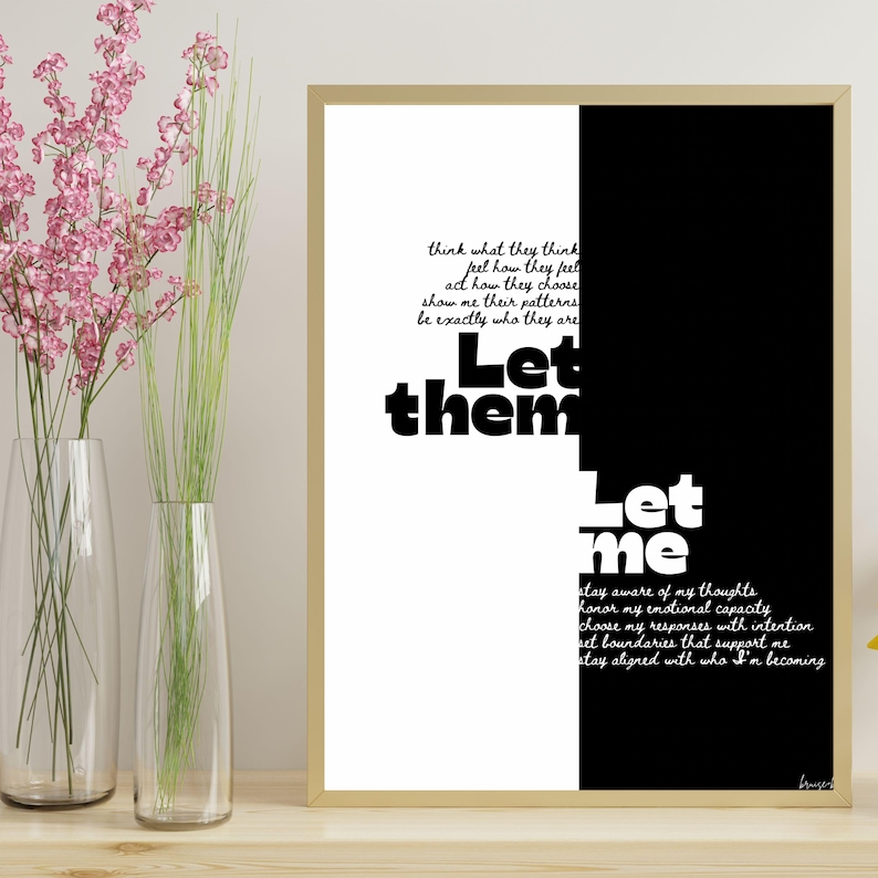 May include: A framed art print with a gold border. The artwork is split vertically, with a black and white design. The text reads "Let them" and "Let me" with inspirational phrases. Two clear vases with pink and green plants are in the foreground.