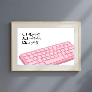 May include: A framed print featuring a pink keyboard illustration. The text reads "CTRL yourself, ALT your thinking, DEL negativity" in black script. The artwork is set against a white background, framed in a light wood frame, and displayed on a gray wall.