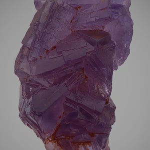 May include: A close-up of a purple fluorite crystal formation. The crystal has a layered, geometric structure with a mix of dark and light purple hues. Some areas show hints of orange and brown.