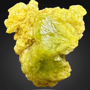 Könnte beinhalten: Nahaufnahme einer rauen, unregelmäßig geformten Mineralprobe. Das Mineral hat eine leuchtend gelb-grüne Farbe, eine kristalline Struktur und ein leicht durchscheinendes Aussehen. Die Oberfläche hat eine strukturierte, unebene Qualität.