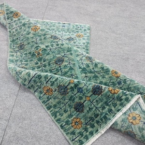 May include: A rolled-up, rectangular rug with a floral pattern. The rug features a teal green background with a repeating pattern of yellow and blue flowers. The edges have a white fringe.