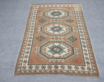Puede incluir: Una alfombra rectangular de estilo vintage con un patrón geométrico. La alfombra presenta un campo de color terracota con formas geométricas repetidas en verde azulado, crema y marrón. El borde tiene un fondo crema con formas de estrella.