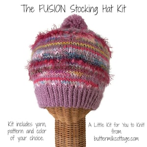 May include: A pink and multi-colored knit stocking hat with a pom-pom on top. The hat is on a wooden stand. The text "The FUSION Stocking Hat Kit" is at the top of the image. The text "Kit includes yarn, pattern and color of your choice." is at the bottom left of the image. The text "A Little Kit for You to Knit! from buttermilkcottage.com" is at the bottom right of the image.