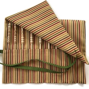 May include: A striped fabric roll-up case with a green ribbon closure, containing a set of wooden knitting needles.