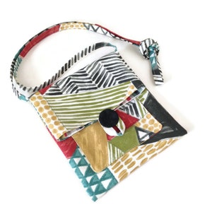 May include: A colorful patchwork crossbody bag with a black button closure. The bag features a variety of patterned fabrics in red, green, gold, black, and white. The adjustable strap is patterned with red, black, and white designs.