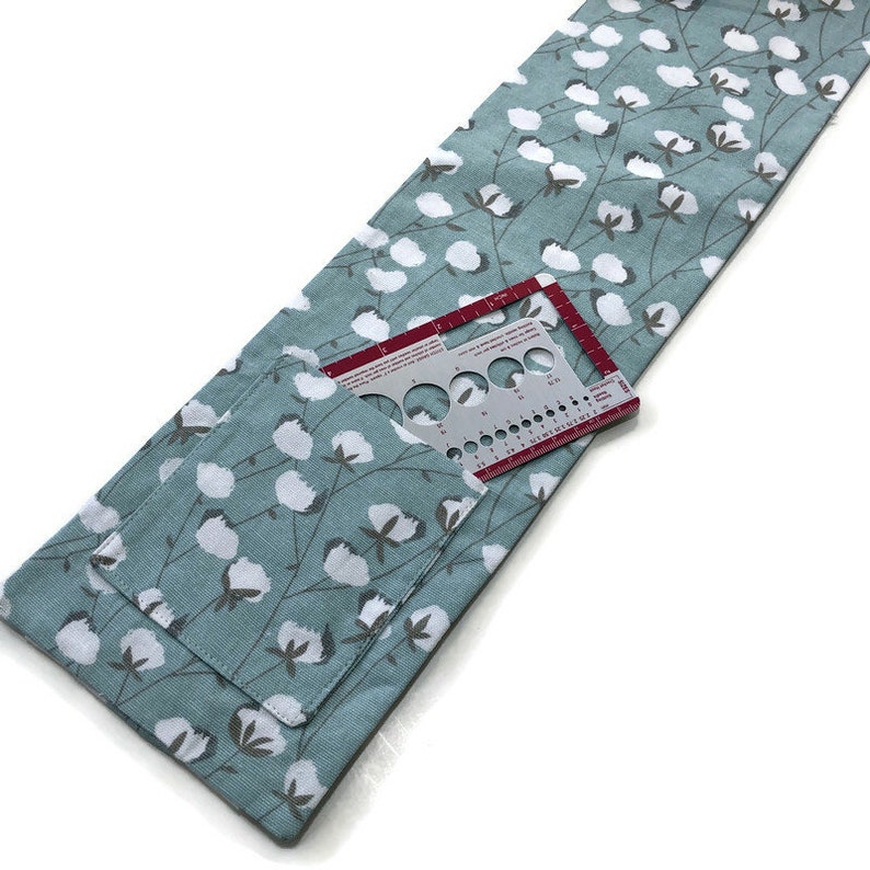 May include: A light blue fabric storage pouch with a white cotton flower print. The pouch has a pocket with a red and silver needle gauge inside.