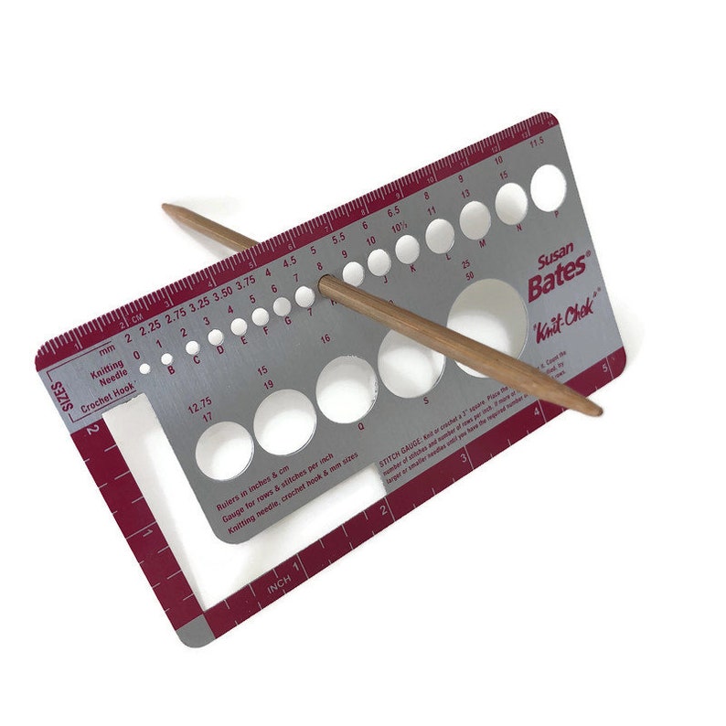 May include: A silver knitting needle gauge with a red border and a wooden knitting needle. The gauge has a ruler in inches and centimeters, and a series of holes for different needle sizes. The gauge is labeled "Susan Bates Knit-Chek".