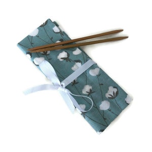 May include: A blue fabric pouch with a white cotton flower pattern and a white ribbon tied around it. Two wooden chopsticks are on top of the pouch.