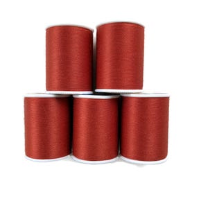 May include: Five spools of red thread are stacked against a white background. The thread is a deep, rich red color, and each spool has a white base and top. The spools are arranged in a pyramid shape, with three on the bottom and two on top.