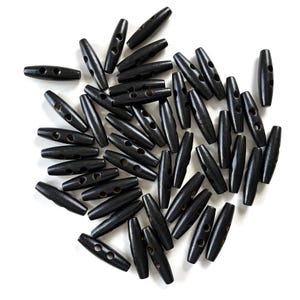 May include: A collection of black wooden toggle buttons, each with two holes for sewing. The buttons are oval-shaped and have a smooth, polished finish. They are scattered on a white background, creating a visually appealing arrangement.