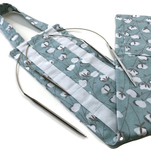 May include: A light blue fabric bag with a white cotton floral print and a white stripe down the center. The bag has a handle and is designed to hold knitting needles. Two silver knitting needles are in the bag.
